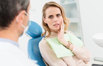 Concerned woman with dental pain sitting in a dental chair and explaining the issue to the dentist.