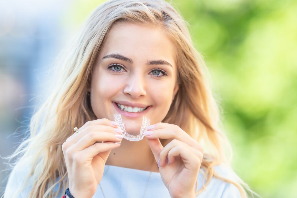 Young smiling woman holding invisalign aligner