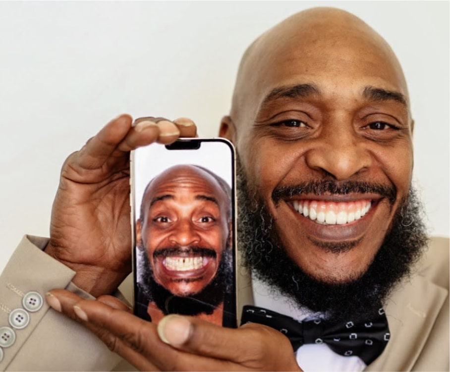 Person smiling broadly while holding a phone displaying a similar smiling image of themselves.