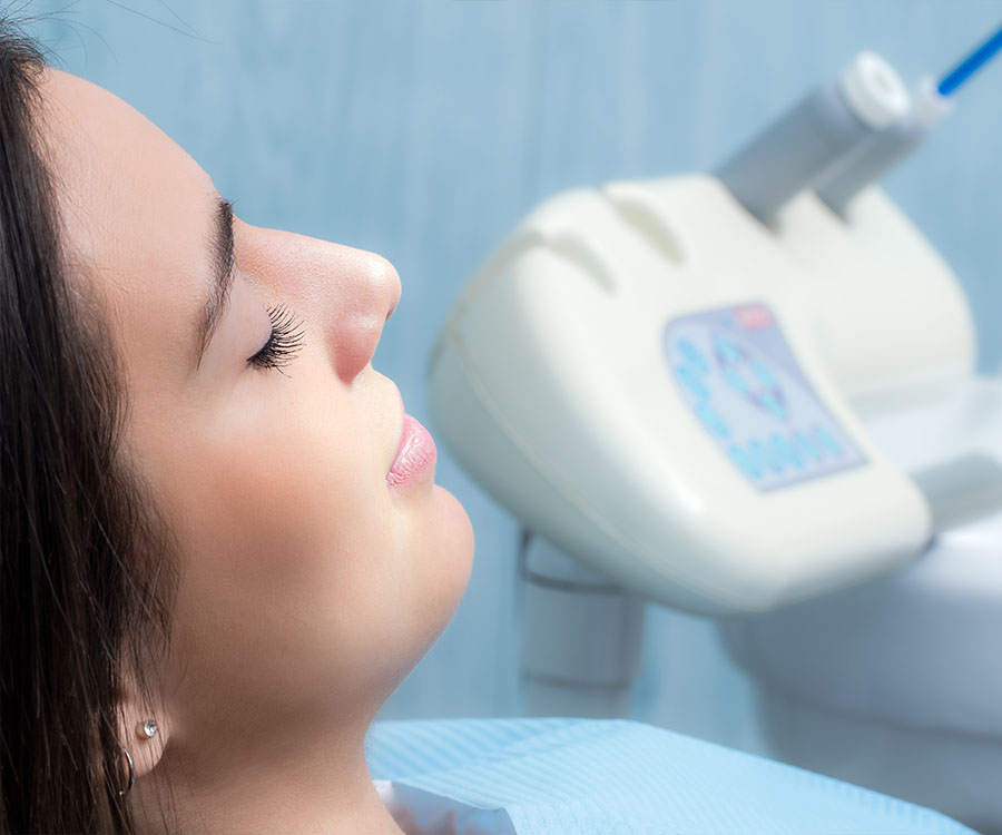 Person reclined with eyes closed in a dental chair, dental equipment in the background.