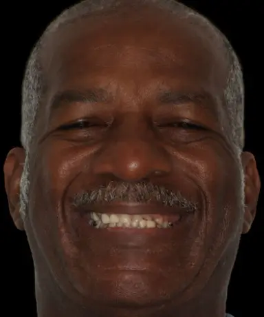 A middle-aged man with short gray hair and a mustache smiles at the camera against a black background.