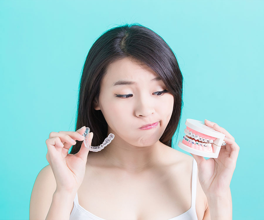 Woman holding a dental retainer in one hand and a dental model in the other, looking thoughtful.