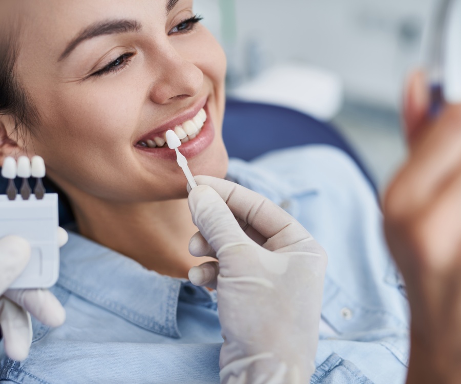 A person at a dental clinic has their teeth shade compared using a shade guide by a gloved dental professional.