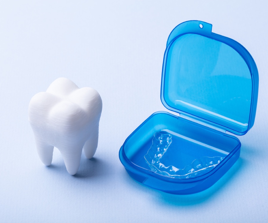 A clear dental aligner in a blue case sits next to a white tooth model on a light blue background.