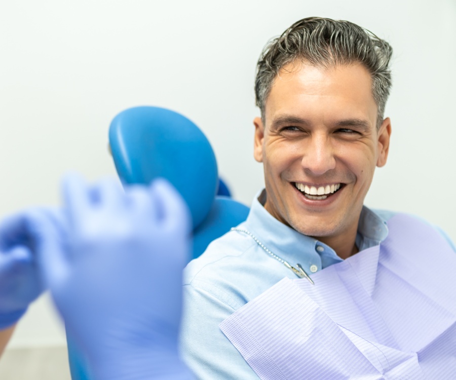 A man sitting in a dental chair smiles at a person wearing blue gloves, suggesting a dental appointment or checkup.