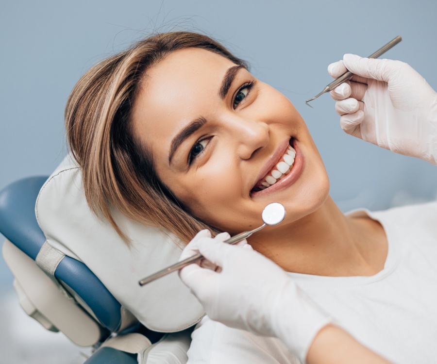 Woman sitting in a dental chair smiling while a dentist holds dental instruments near her mouth.