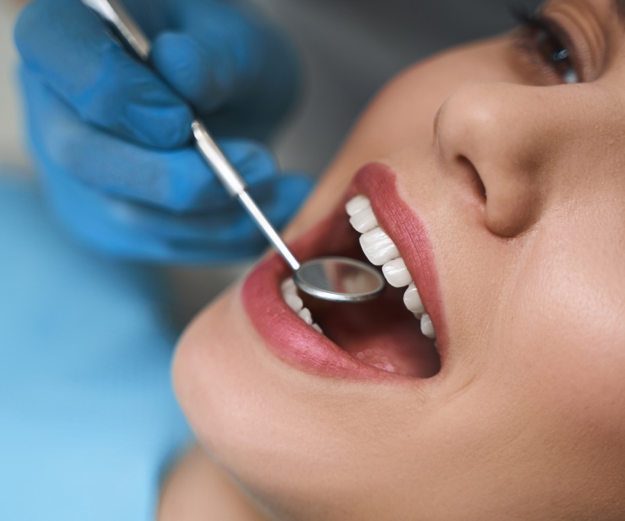 A dentist wearing blue gloves examines a patient's teeth with a dental mirror during a check-up.