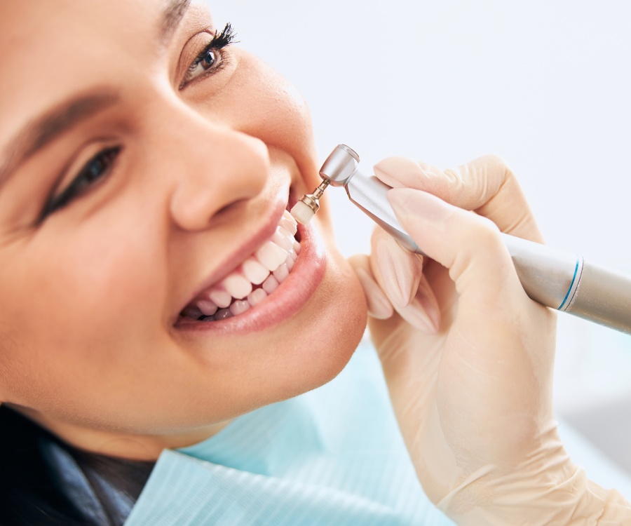 A person at a dental appointment is smiling while a dentist uses a dental tool to clean their teeth.
