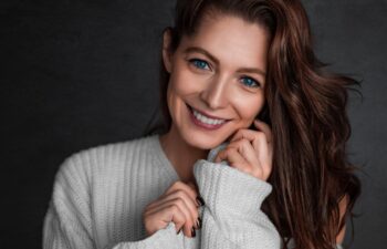 Smiling blue eyed 40 years old woman looking at camera. Photo over dark grey background. Psychology and feminine health concept.