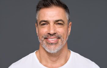 Happy confident handsome healthy mature older man, smiling middle aged male model wearing white t-shirt standing isolated on gray background advertising skin care and dental smile concept.