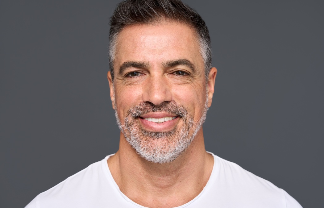 Happy confident handsome healthy mature older man, smiling middle aged male model wearing white t-shirt standing isolated on gray background advertising skin care and dental smile concept.