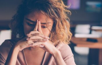 Closeup of sad young Asian woman at cafe leaning head on clasped hands and staring into vacancy.