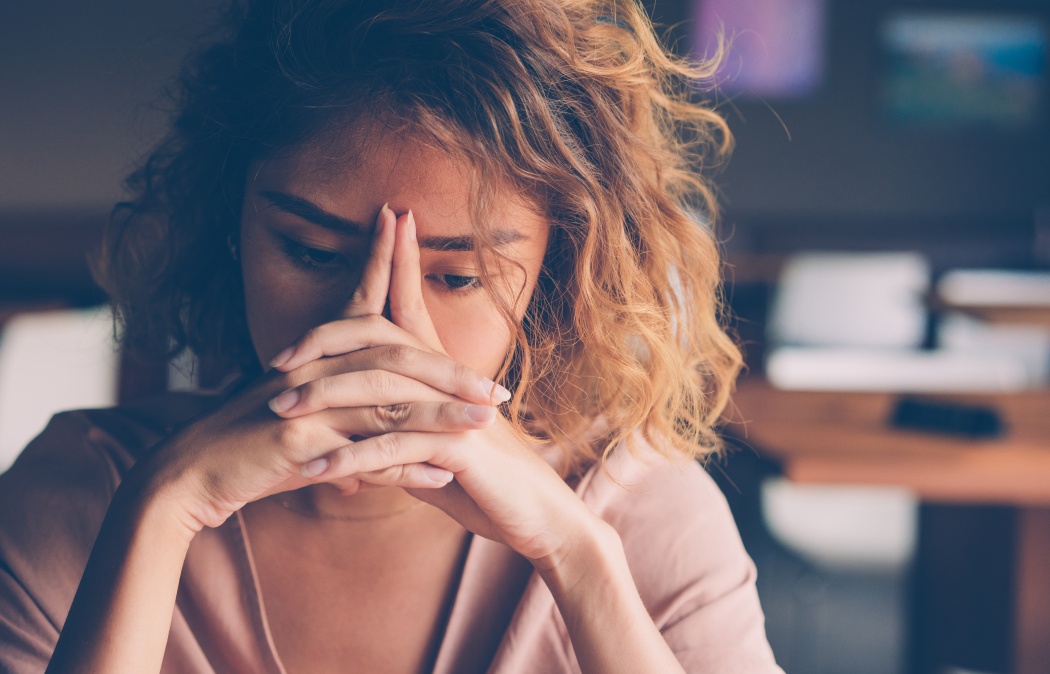 Closeup of sad young Asian woman at cafe leaning head on clasped hands and staring into vacancy.